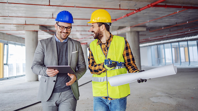 Smiling architect with helmet on head talking to contractor in a construction site