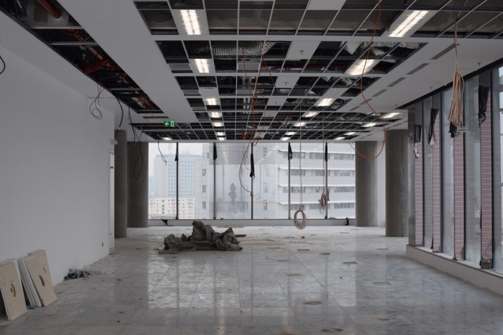 An empty office space featuring construction equipment and a large window allowing natural light to enter.