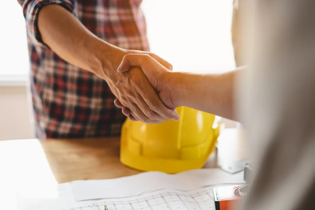 Contractor and client / engineer shaking hands after deal to renovation building is complete and blueprint is reviewed.
