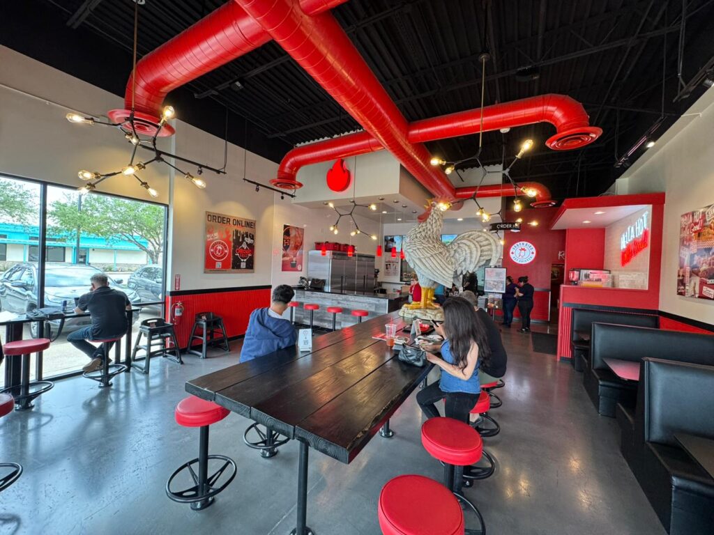 A restaurant interior featuring red and black pipes, complemented by red stools arranged around tables.