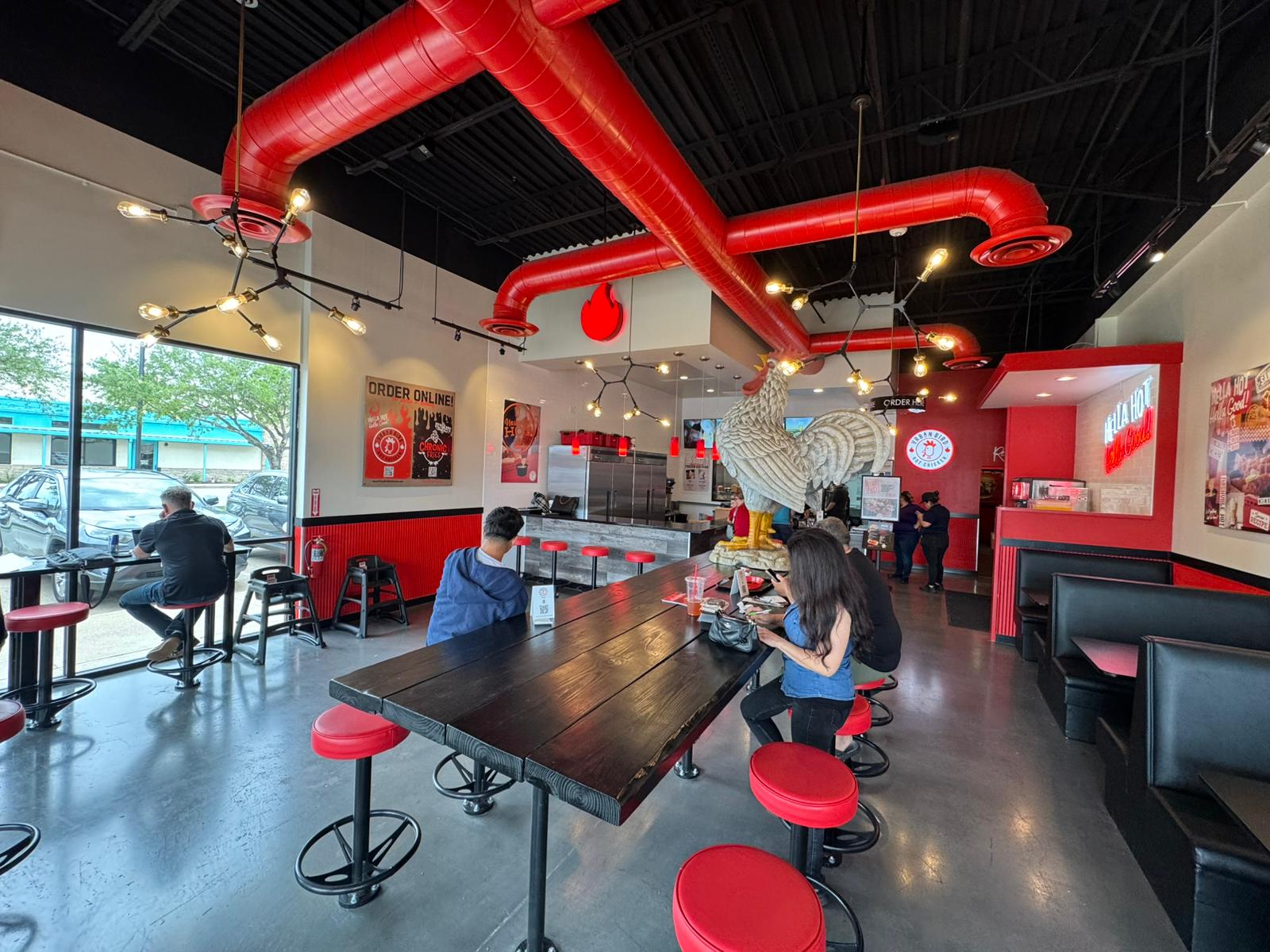 A restaurant interior featuring red and black pipes, complemented by red stools arranged around tables.